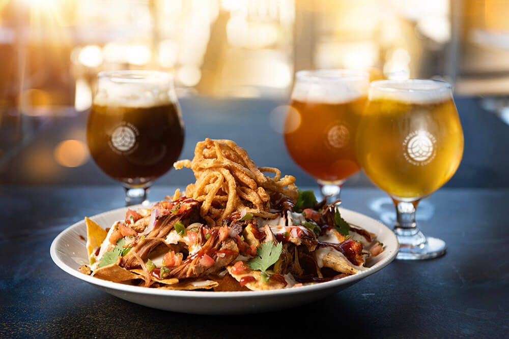 plate of nachos alongside tangled roots beers