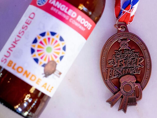 Great American Beer Festival bronze medal next to Tangled Roots Sunkissed Blonde Ale bottle