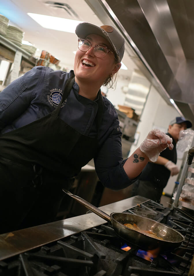 Woman chef smiling while seasoning food on a flaming grill