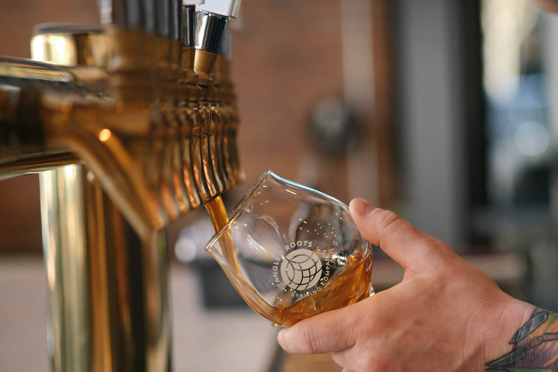 close up of a row of beer taps with beer being poured into a Tangled Roots glass